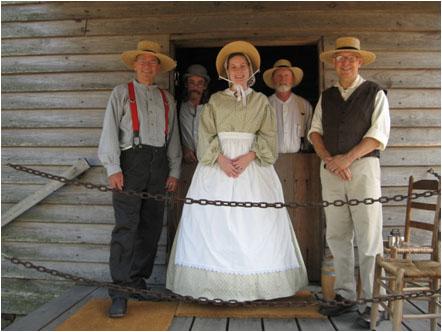 Group of costumed volunteers stand together in front of old wooden mill