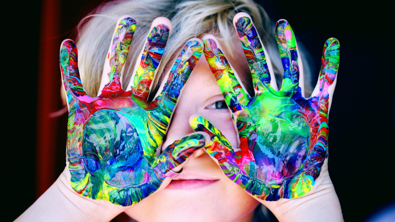 Child with colorful paint on their hands held in front of their face