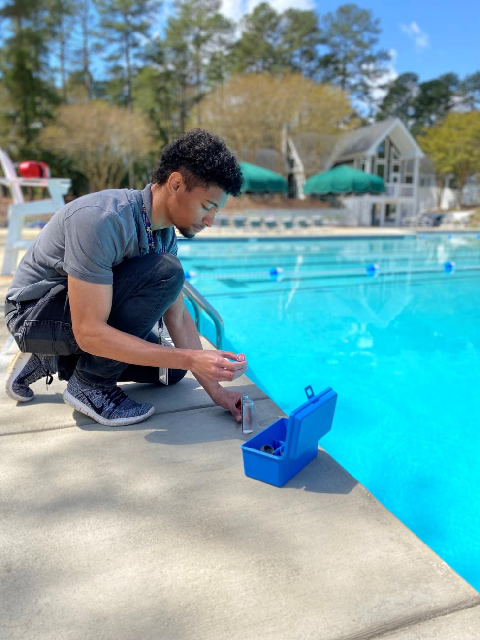 Environmental health specialist kneels poolside with a kit to test the pool water