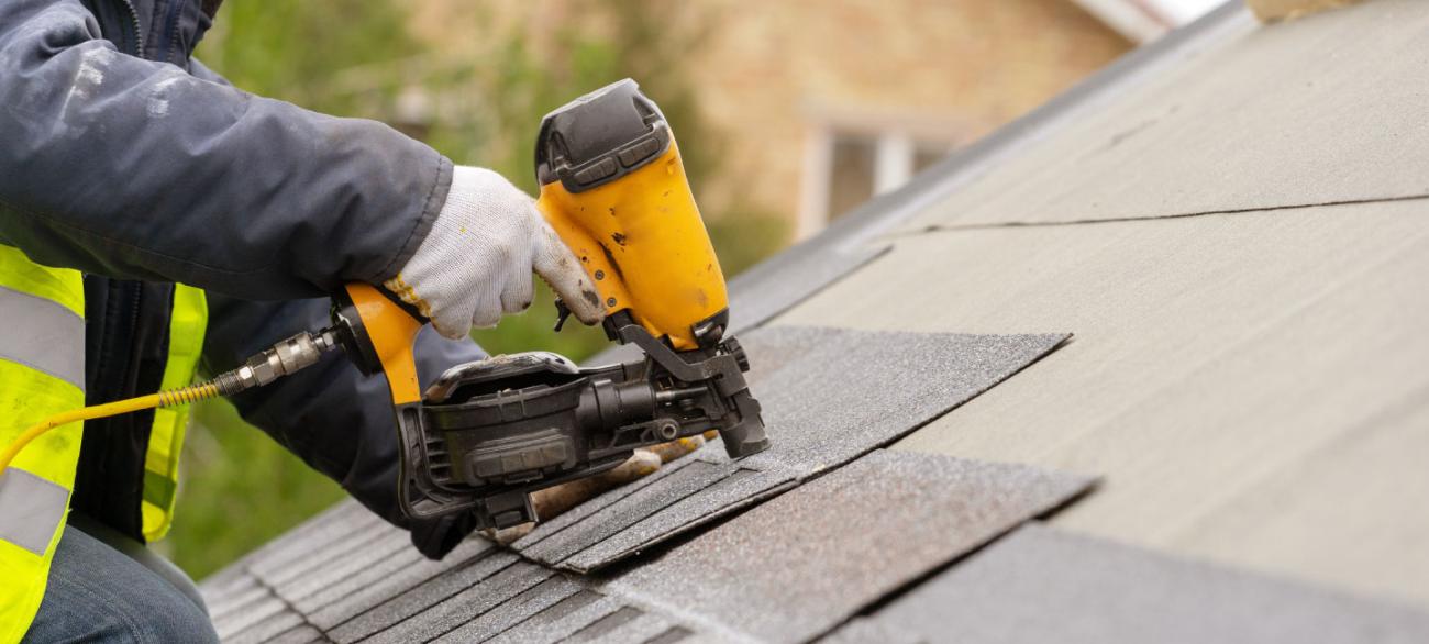 worker nailing roof shingles