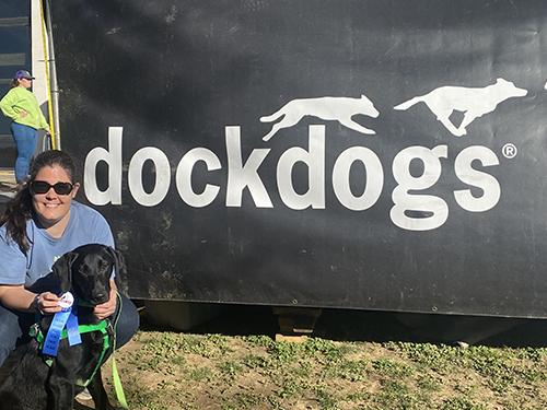 Dr. Jennifer Federico kneels with Miller the dog and his first-place ribbon in front of a DockDogs canvas