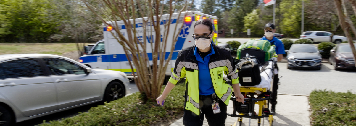 Paramedics wheeling a gurney out of an emergency vehicle.