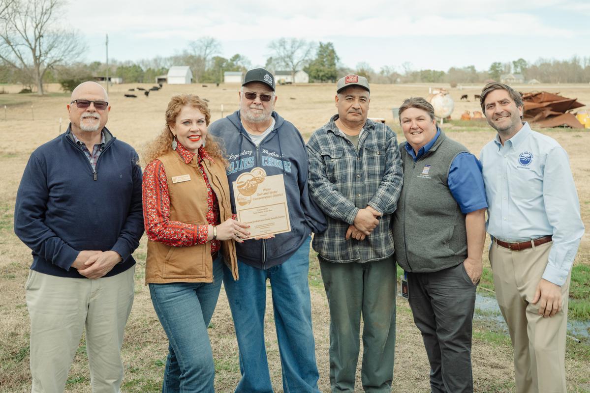 Soil and Water supervisors and director present award to farmers standing in field