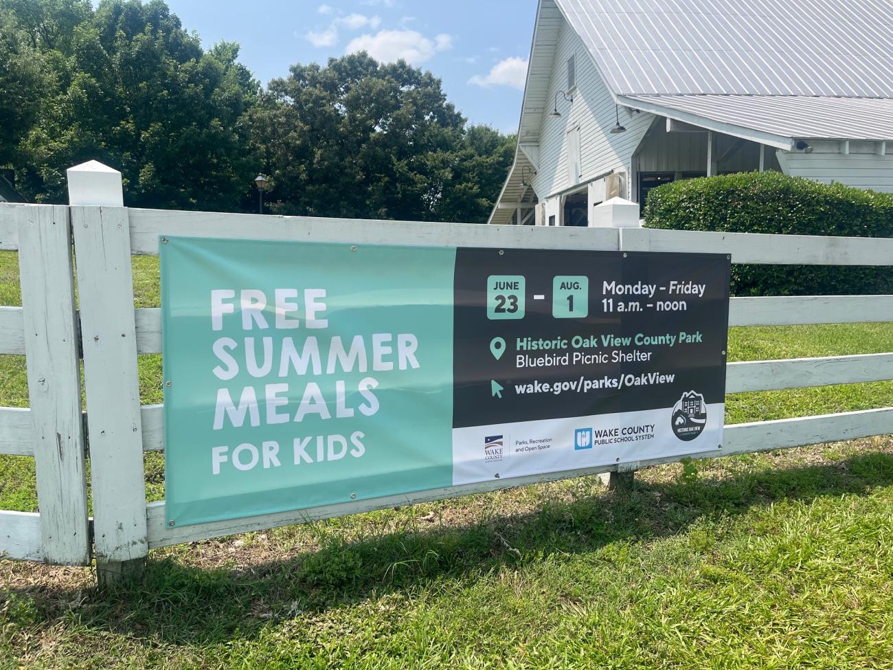 Banner hanging on a white fence, showing details of the 2025 Summer Food program