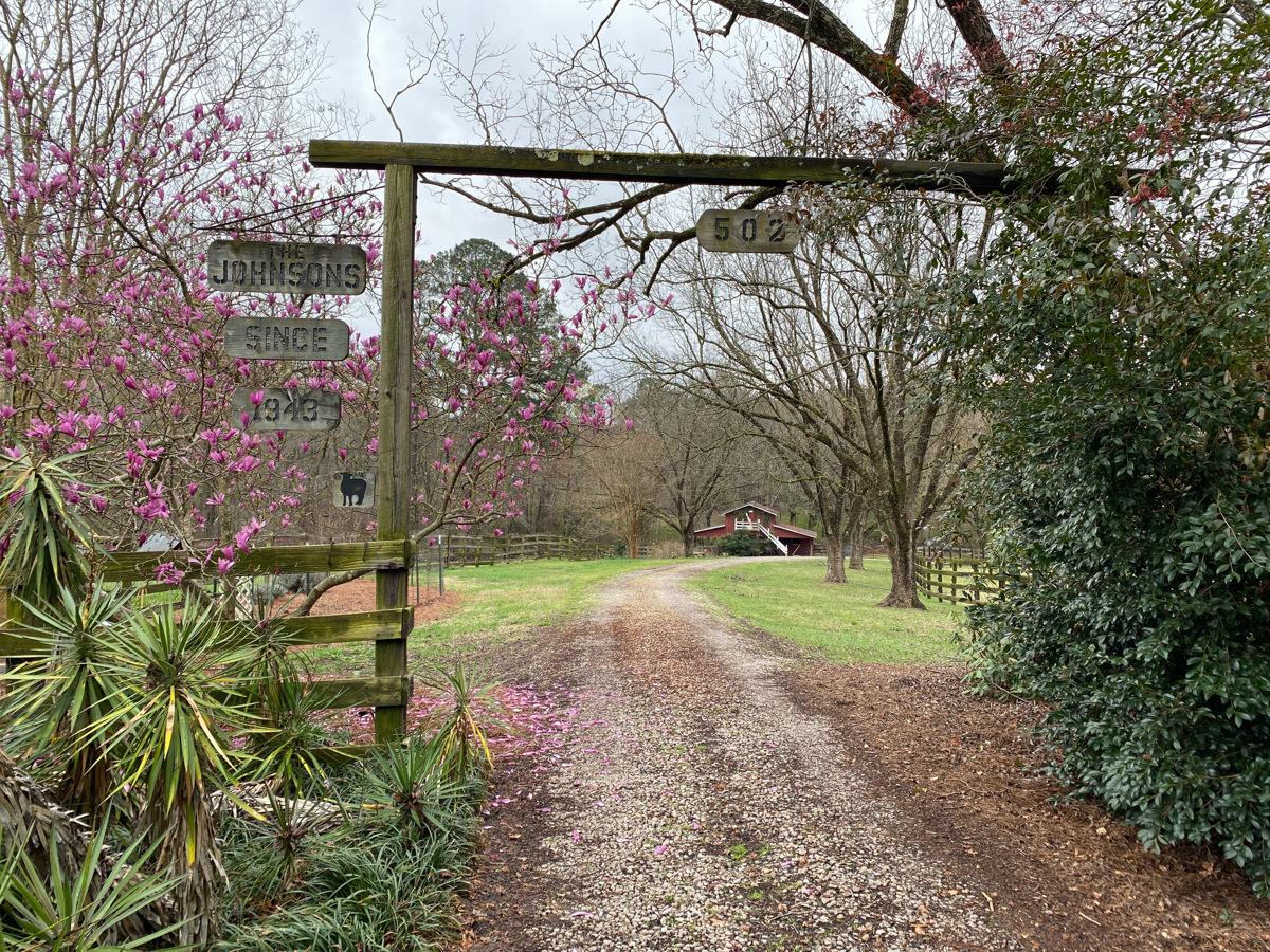 wooden archway entrance and path surrounded by trees and plants with barn in background