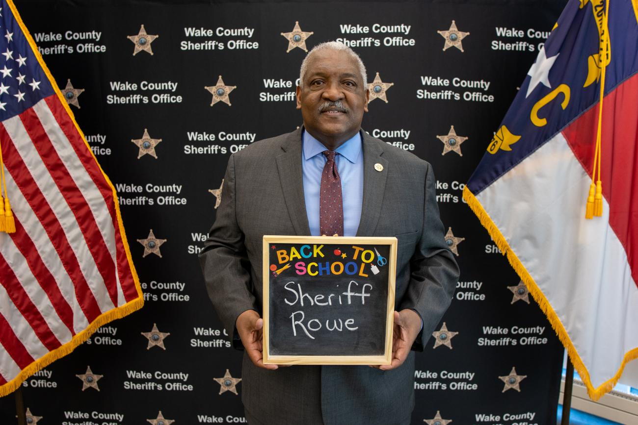 Sheriff Rowe holding a chalkboard that says "Back to School, Sheriff Rowe"
