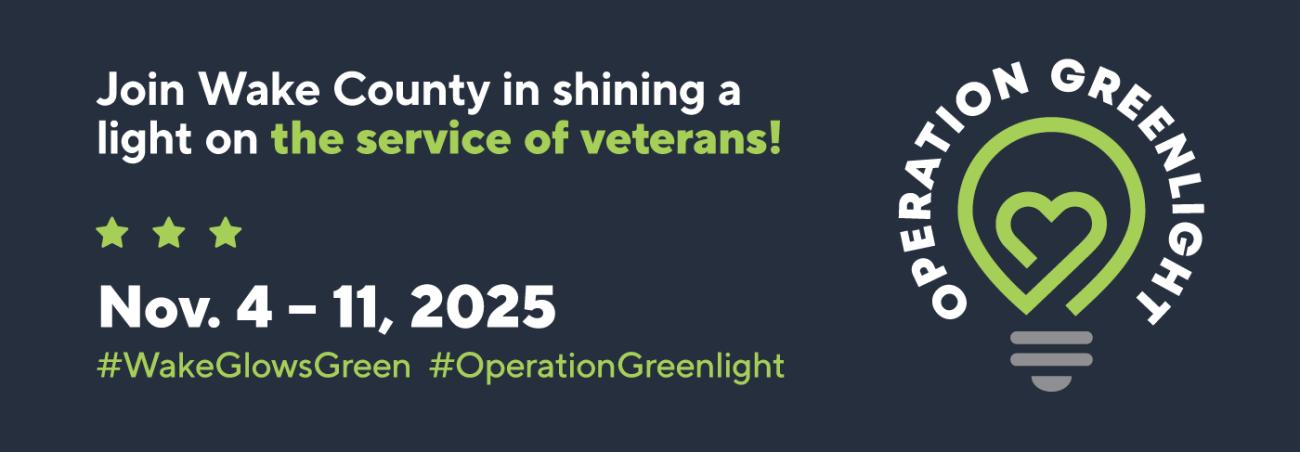 Operation Greenlight promotional banner. Text reads: ‘Join Wake County in shining a light on the service of veterans! Nov. 4–11, 2025. #WakeGlowsGreen #OperationGreenlight.’ To the right is a green heart inside a light bulb, with the words ‘Operation Greenlight’ surrounding the logo.