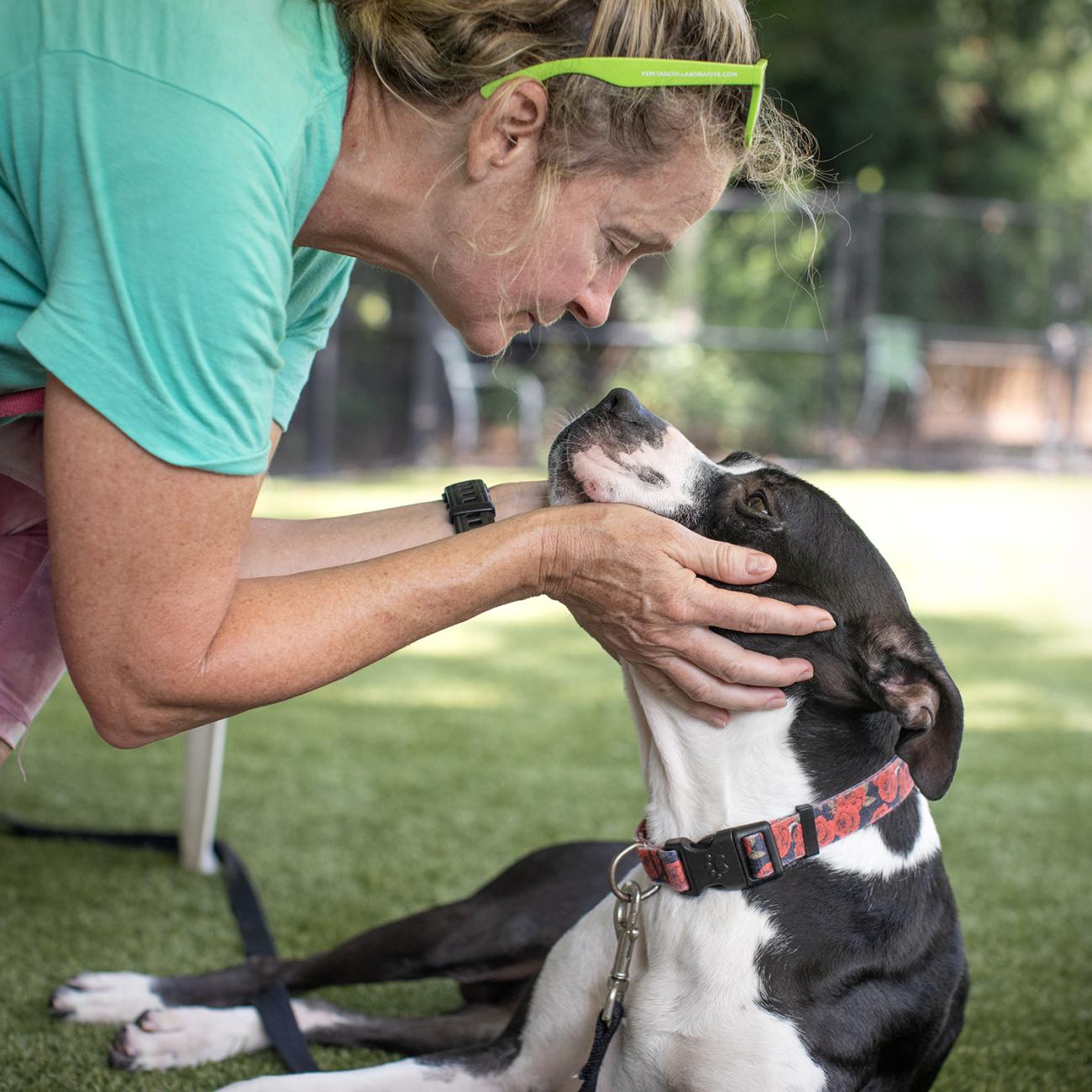 Christine kneels to connect nose-to-nose with a black-and-white dog in the play yard.