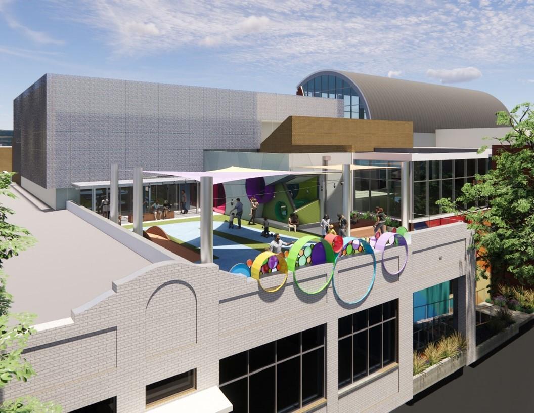 Elevated view of a rooftop courtyard on a modern building, featuring colorful circular art elements along the edge, shade canopies, and play or seating areas.