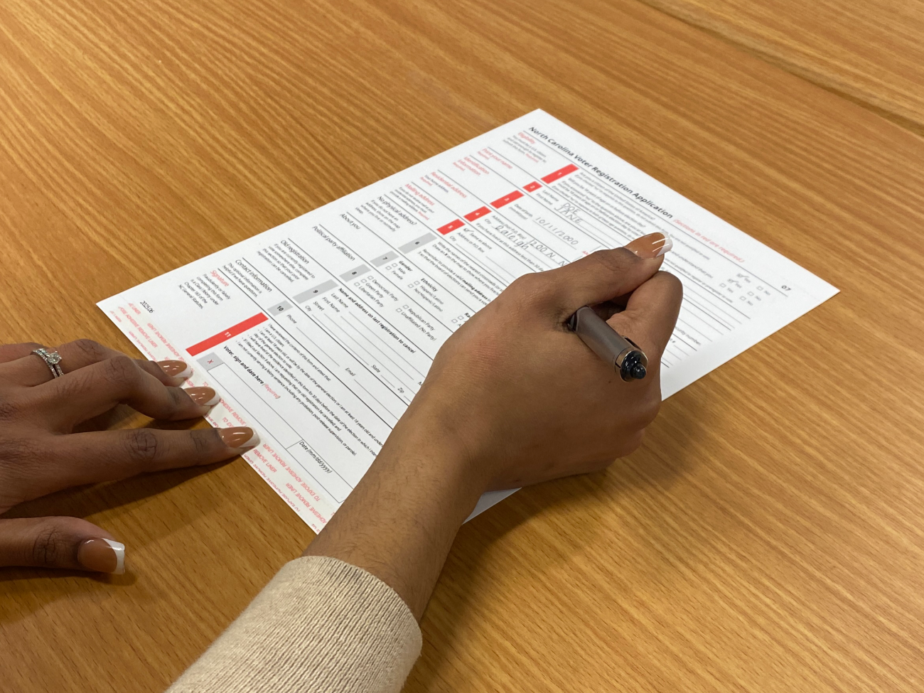 Hands filling out a voter registration form on a wooden table.