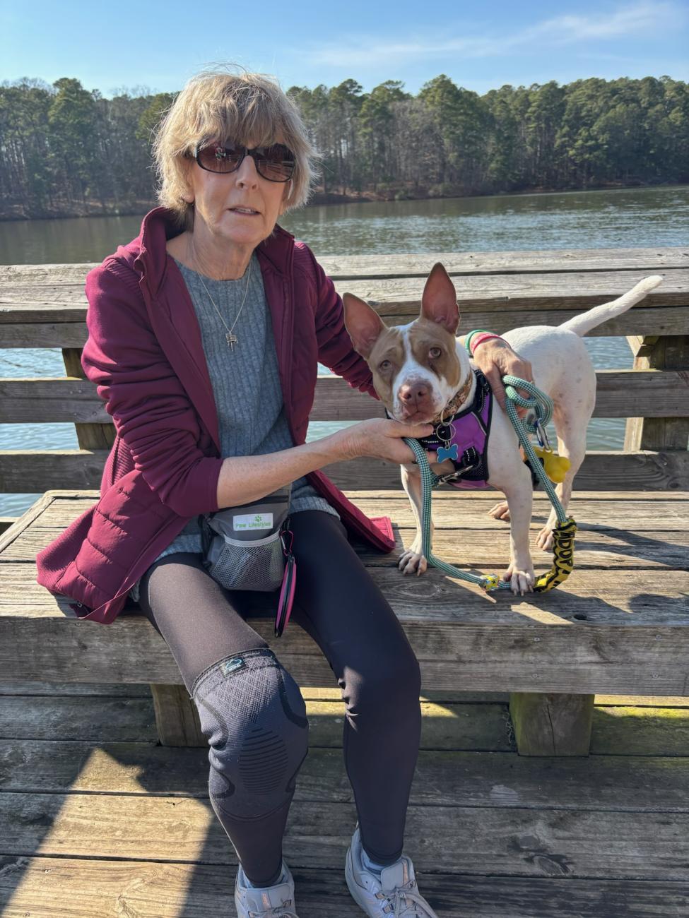 Wake County foster Kim Leon sitting on a dock with a foster dog on leash beside a lake.