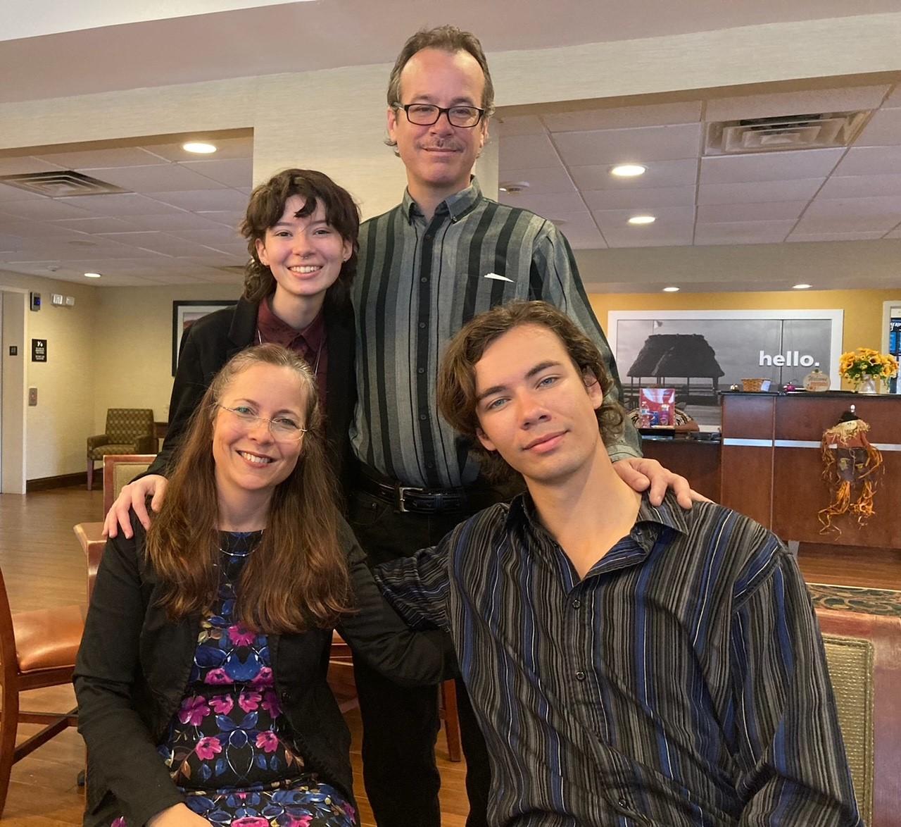 Four people smiling together indoors, posed for a group photo.