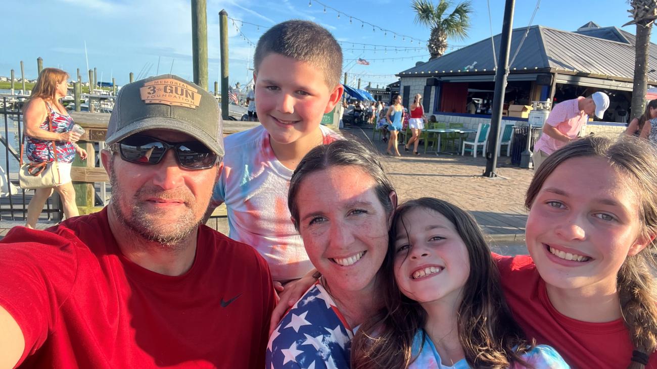 Family selfie outdoors near a waterfront restaurant.