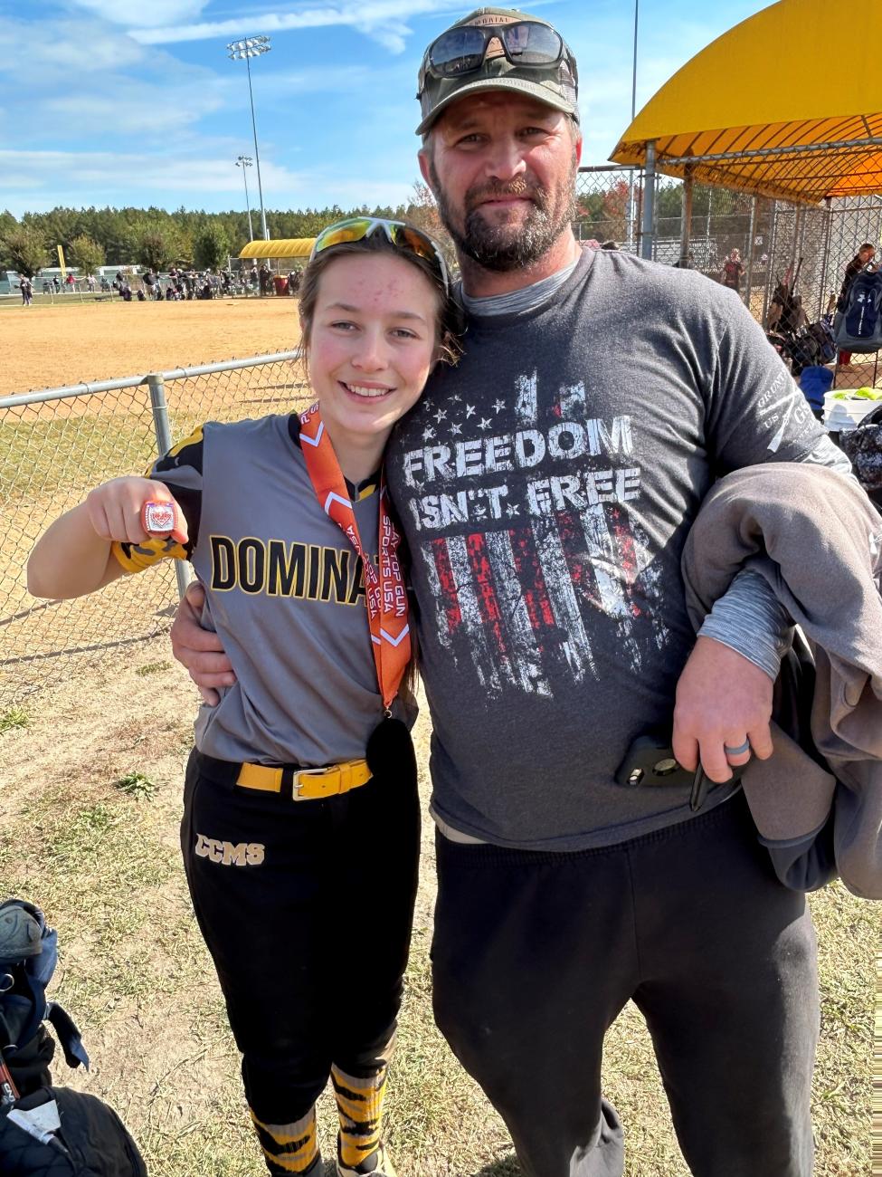 Softball player wearing a medal posing with an adult on a field.