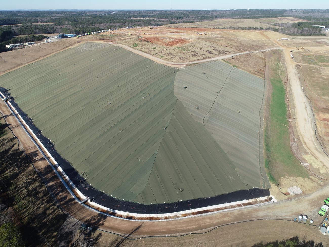 Aerial view of a landfill with a large completed interim cover, surrounded by dirt roads and open land.