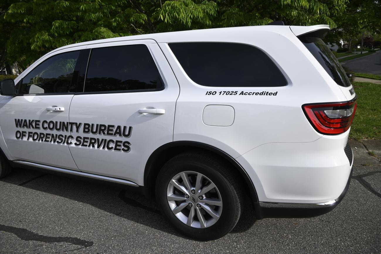 A white car with black text on its side that reads: Wake County Bureau of Forensic Services, ISO 17025 Accredited