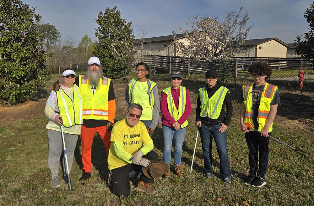 Group of volunteers in safety vests pose outdoors with litter pickers during a community cleanup event.