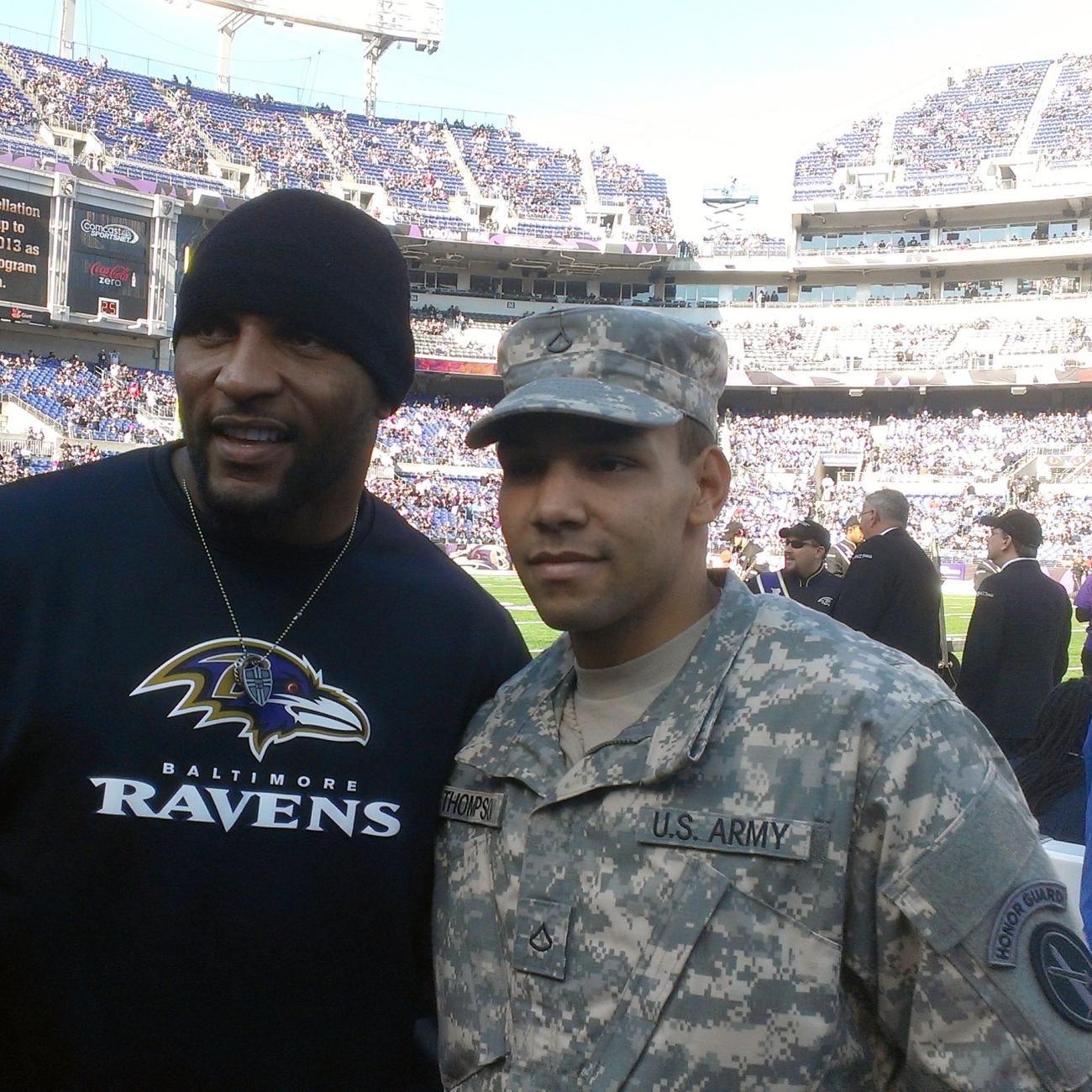 Man in Army Honor Guard fatigues poses with man in Baltimore Ravens sweatshirt inside a large stadium.