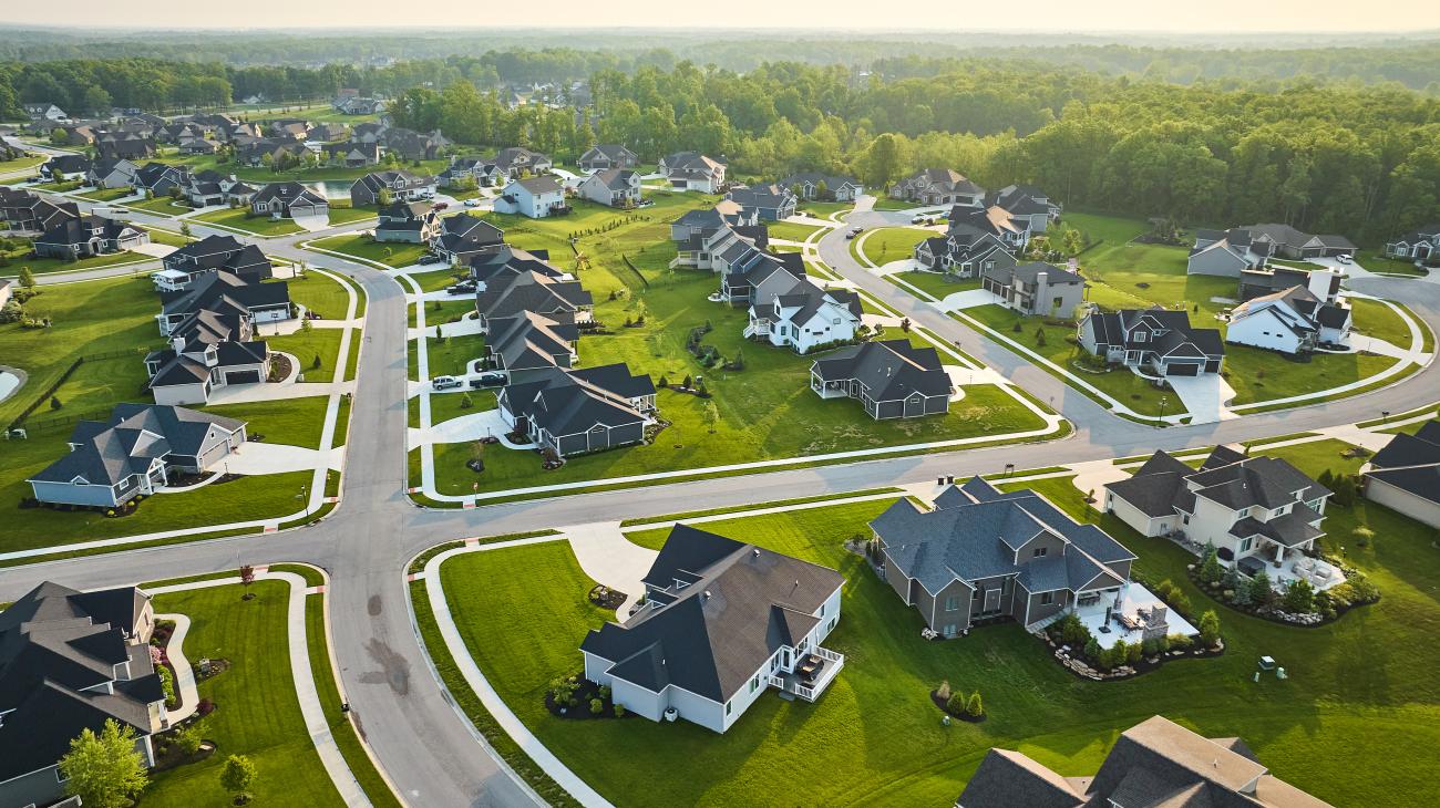 Aerial view of a residential subdivision with houses, streets, and green lawns arranged in a neighborhood layout.