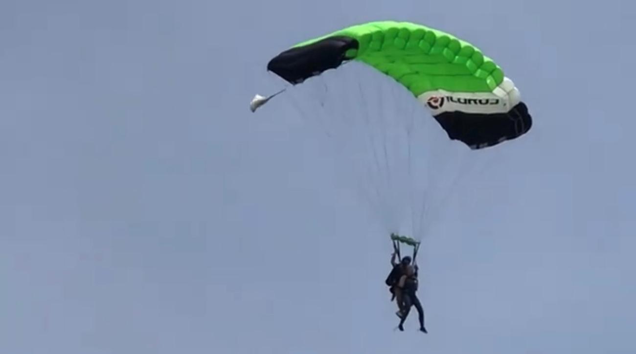 A person descending through the sky using a green-and-black parachute.
