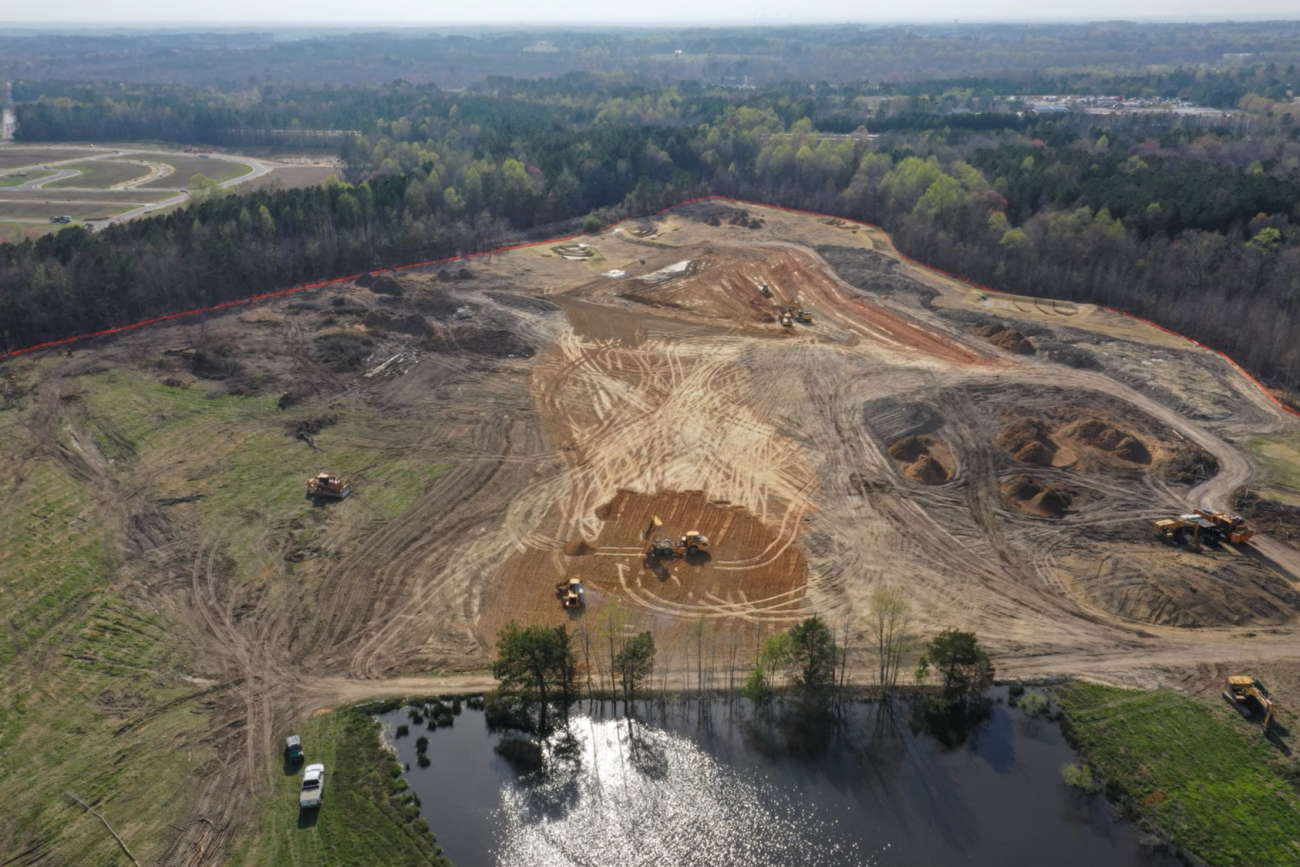 Aerial view of an active land development site with exposed soil near a pond.