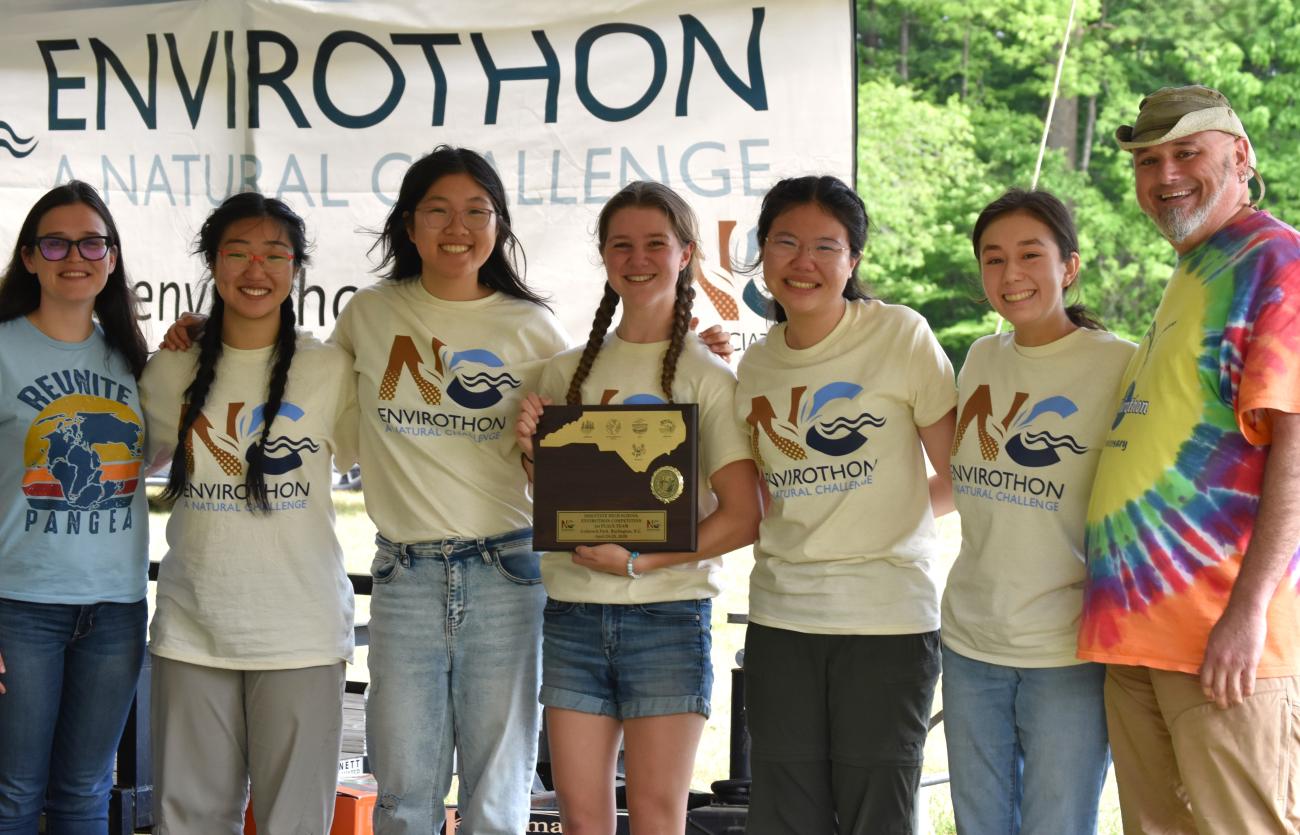 Group of students and adults posing with an award plaque in front of an Envirothon Natural Challenge banner.