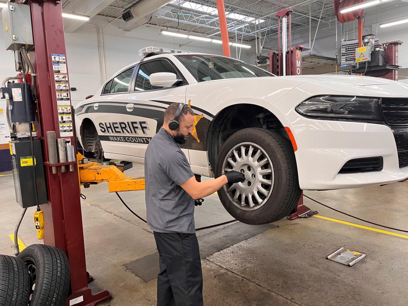 Technician servicing a Wake County Sheriff patrol car on a lift inside a maintenance shop.