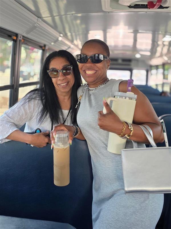 Two women smile together while standing on a bus.