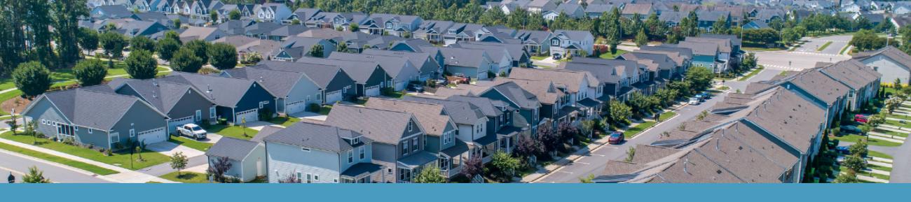 Aerial view of a residential subdivision with houses, streets and green lawns arranged in a neighborhood layout.