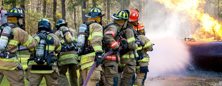 Fire trainees spray a hose on a burning storage tank