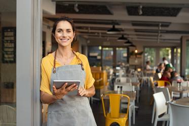 Smiling food server holds tablet while standing in restaurant