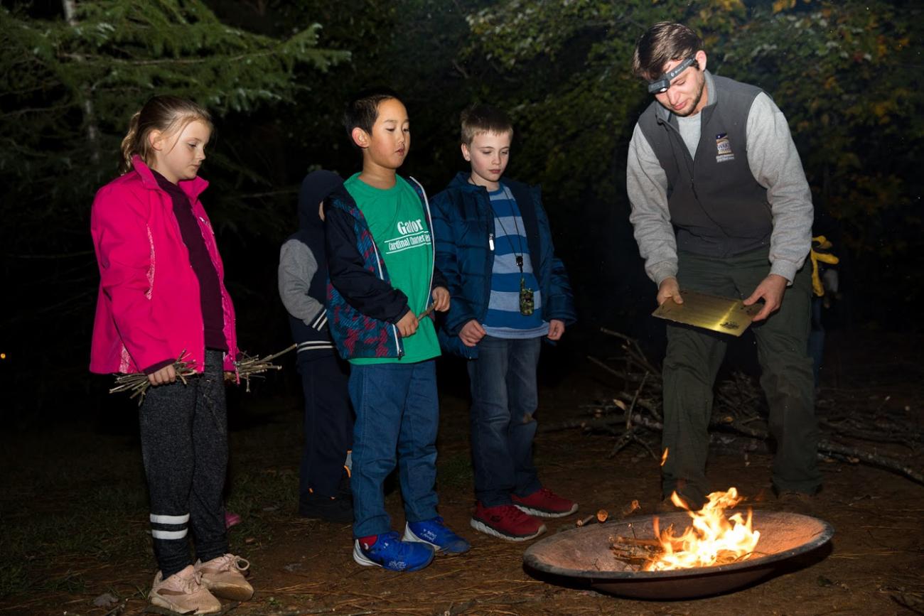 programmer and children stand around firepit during night program