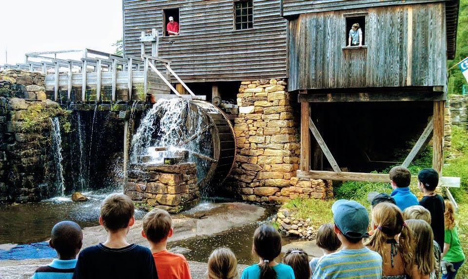 children watch mills waterwheel move by waterfall and dam