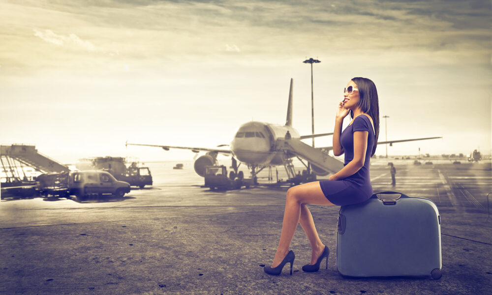 travel-woman-sitting-on-suitcase-in-front-of-plane