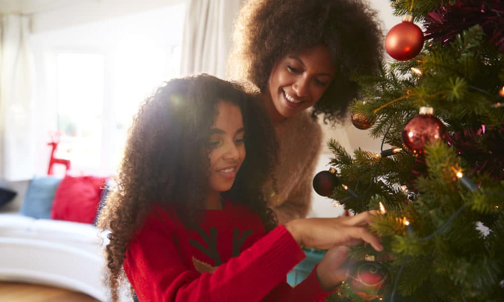 Mother And Daughter Hanging Decorations On Christmas Tree At Home