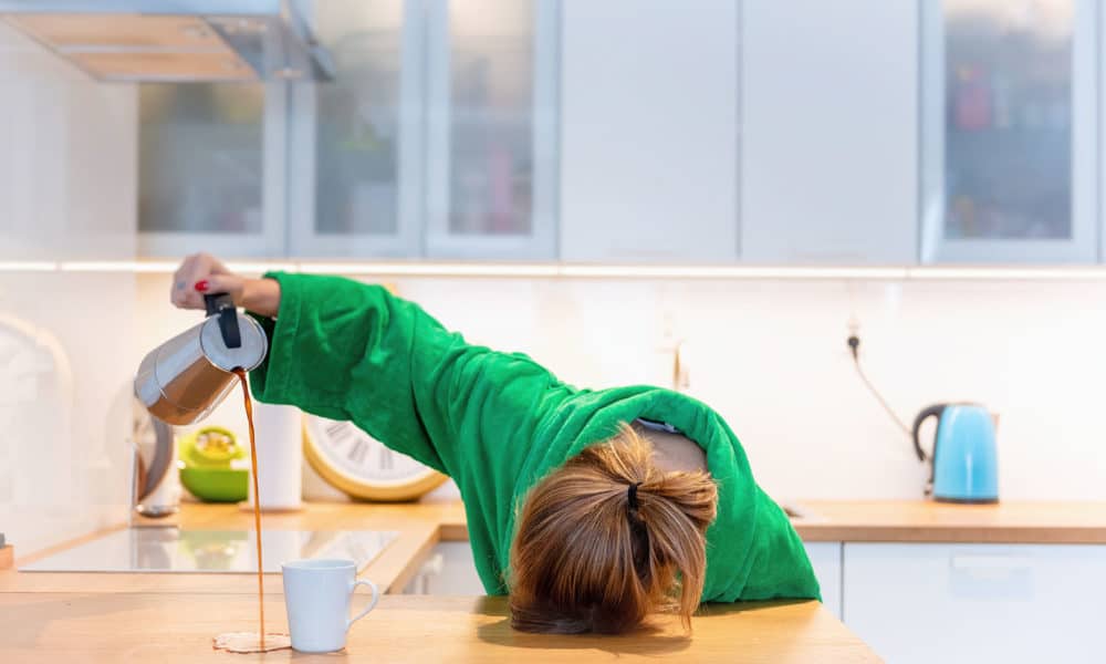 Tired woman sleeping on the table in the kitchen at breakfast. Trying to drink morning coffee