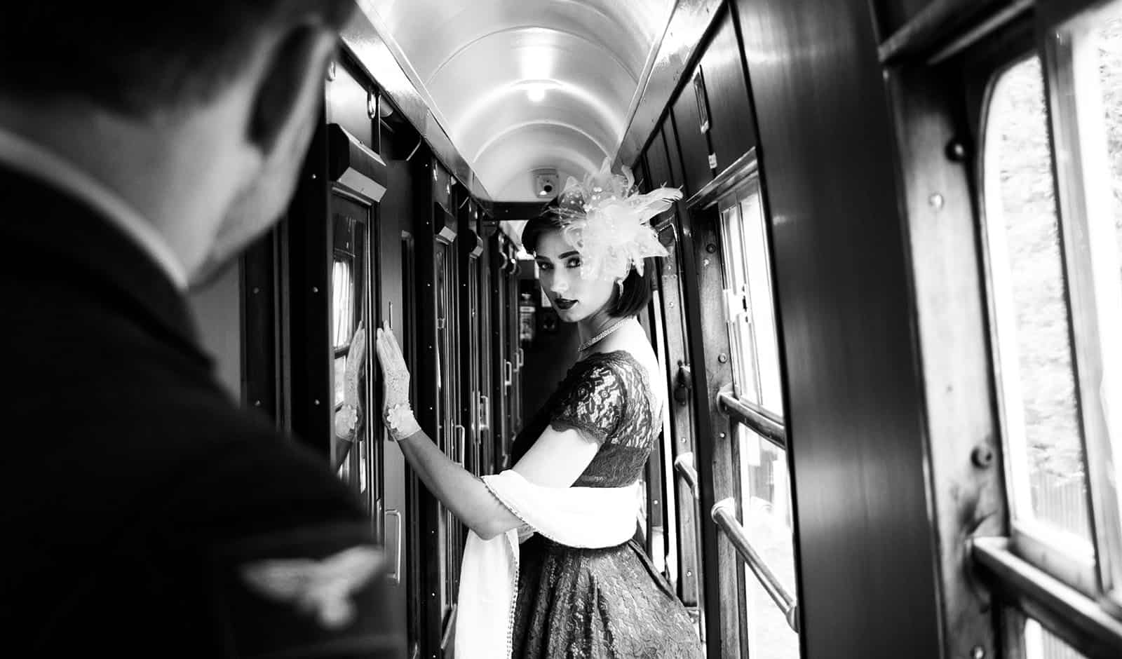 Portrait of beautiful woman in vintage tea dress standing in corridor of locomotive train as air force officer in uniform watches her