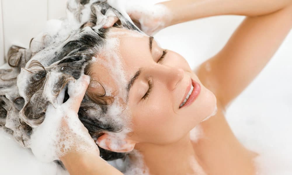 Young and beautiful woman is washing her hair with shampoo