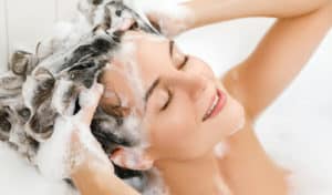 Young and beautiful woman is washing her hair with shampoo